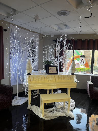 A beautifully decorated lounge area featuring a yellow piano surrounded by festive lighting and decorative trees.