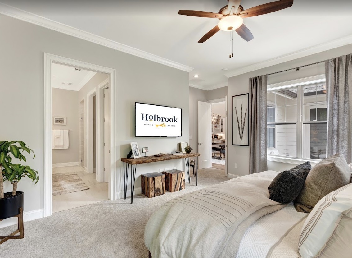 A cozy bedroom with modern decor, featuring a ceiling fan, wall-mounted television, and large windows.