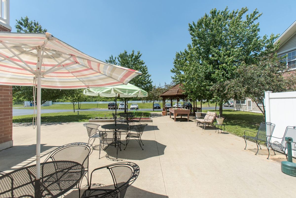 A sunny patio area with tables, chairs, and umbrellas near a gazebo.