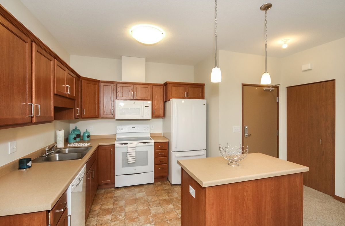 A modern kitchen featuring wooden cabinets, white appliances, and pendant lighting.