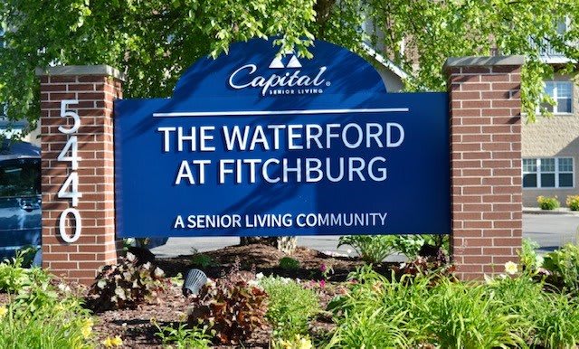 A sign for The Waterford at Fitchburg, a senior living community, surrounded by greenery.