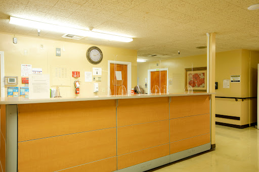 A view of a hospital reception area featuring a wooden counter and a clock on the wall.