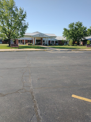 A sunny day view of a well-maintained building surrounded by greenery and a clear parking lot.
