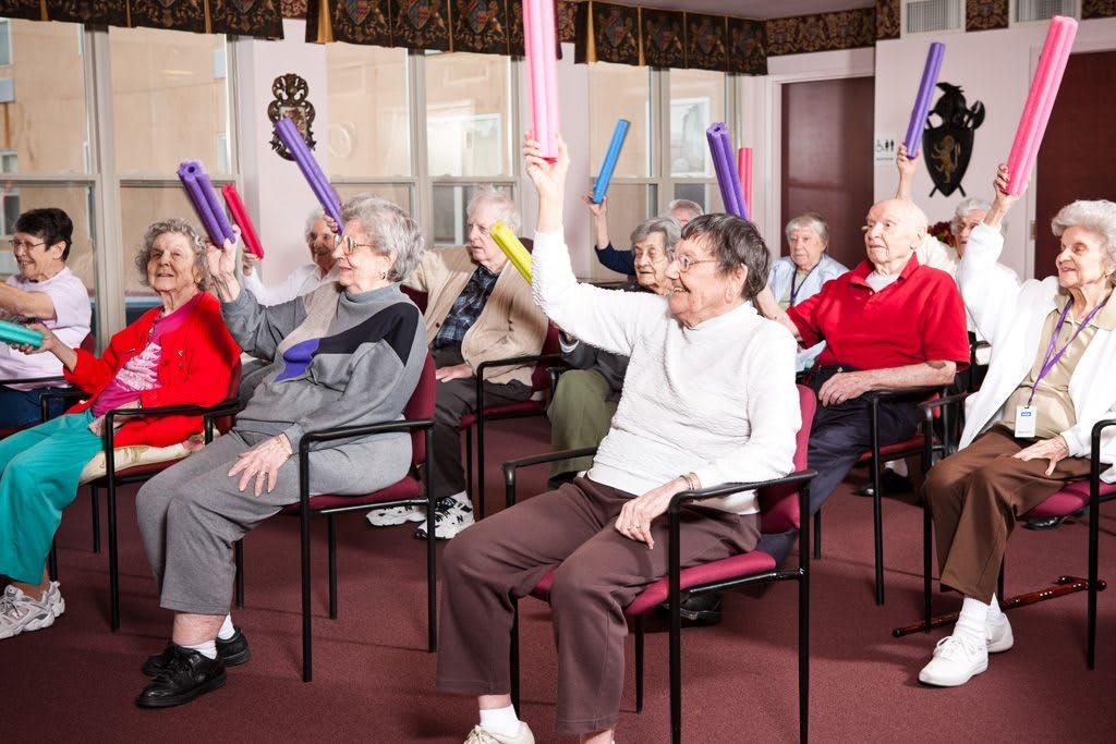 A group of seniors engaging in an indoor exercise class using colorful batons.