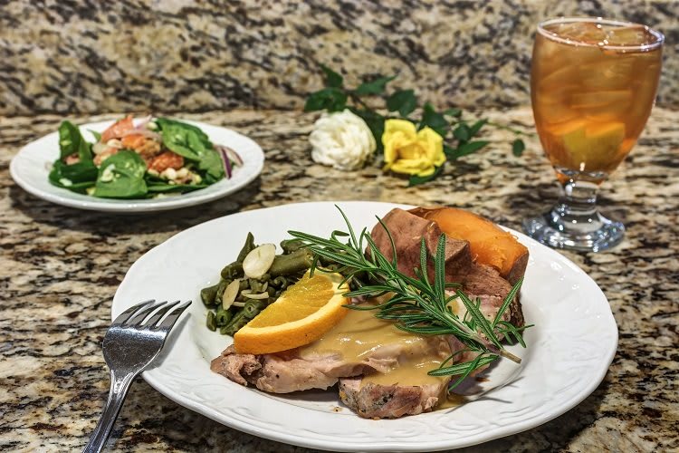 A delicious dinner plate featuring roast meat with orange garnish, vegetables, and a sweet potato, accompanied by a fresh salad and iced tea.