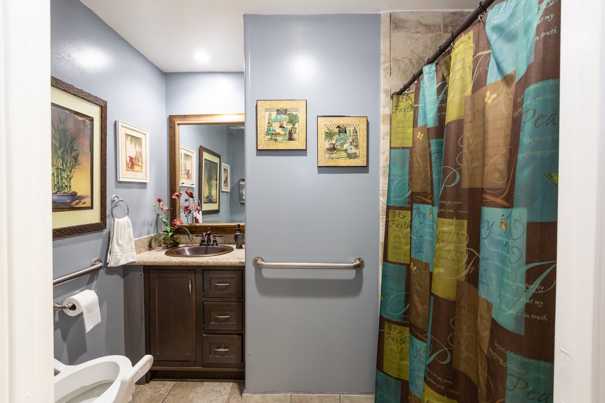 A well-lit bathroom with a mirror, sink, and colorful shower curtain.