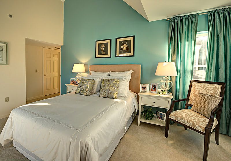A cozy bedroom with a neatly made bed, flanked by nightstands and lamps, featuring warm decor accents.