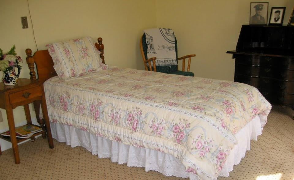 A quaint bedroom with a single bed dressed in floral bedding and a wooden rocking chair in the corner.