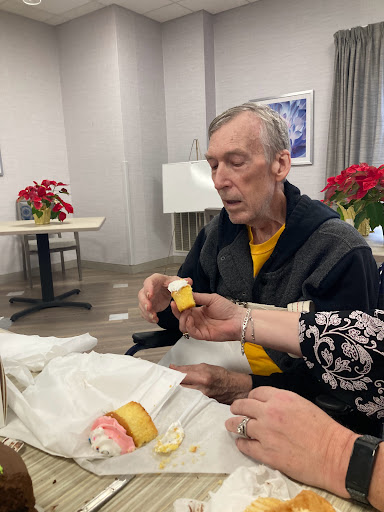 A senior man engaging in an activity with assistance from another person, surrounded by decorative flowers.