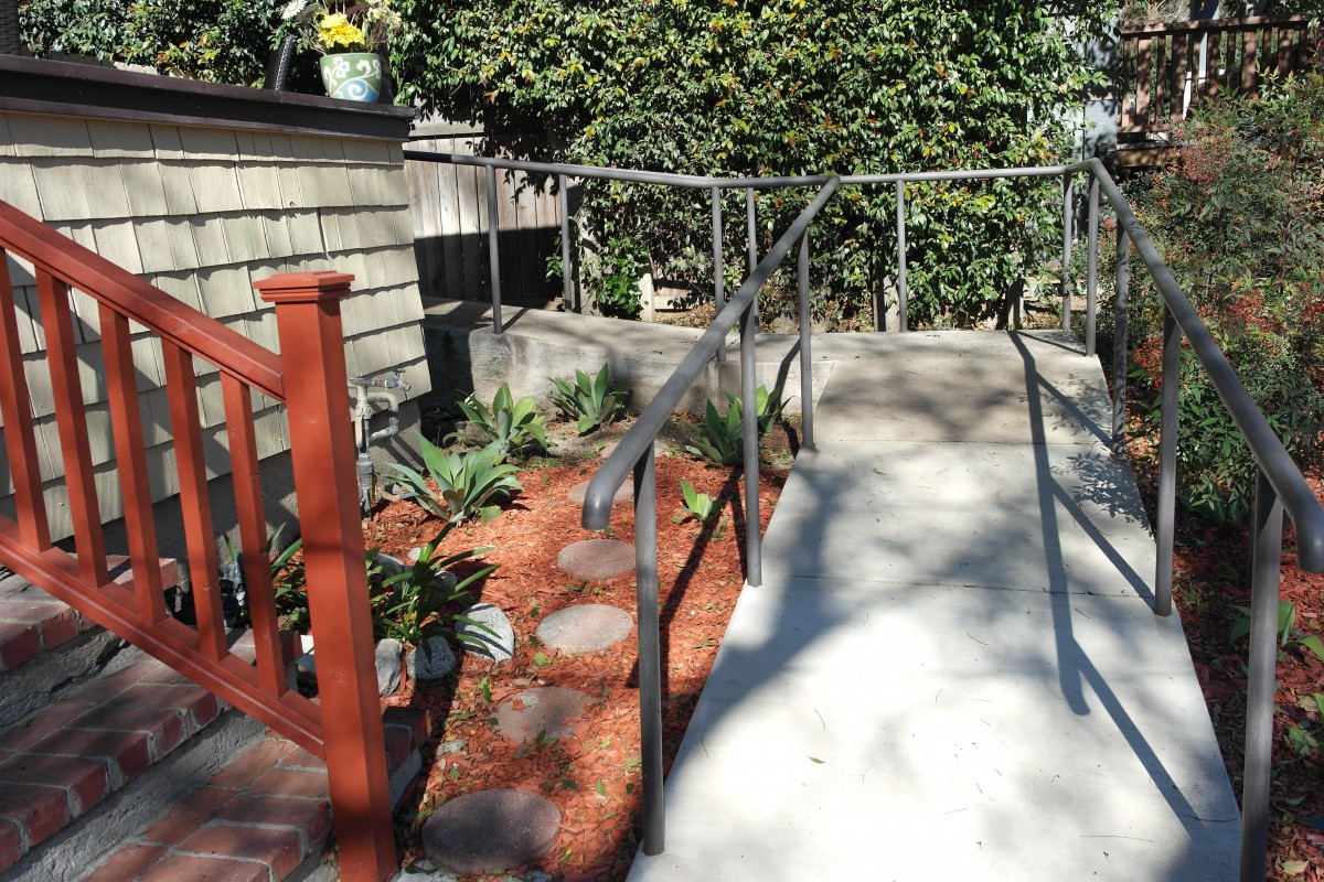An outdoor ramp with handrails leading up to a garden area.