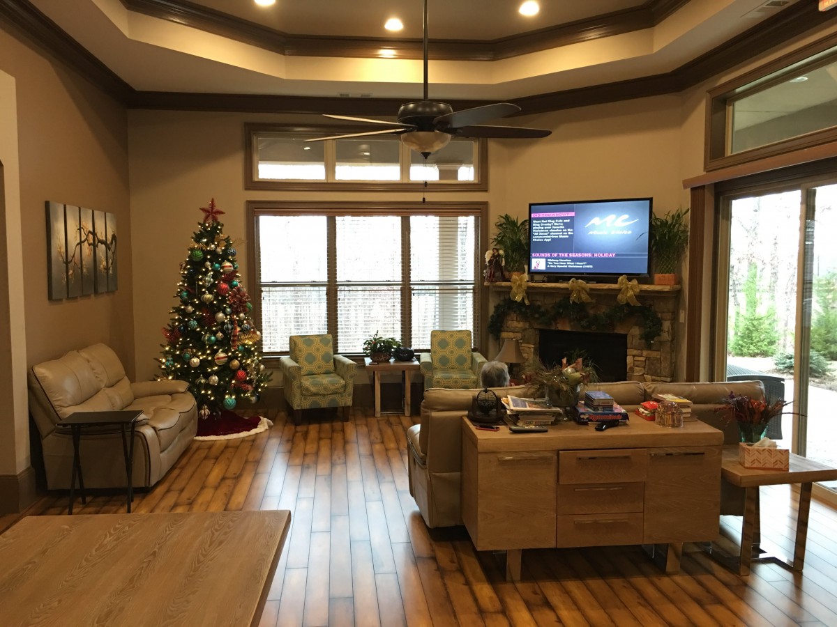 A cozy living room with a Christmas tree, sofas, armchairs, and a fireplace.