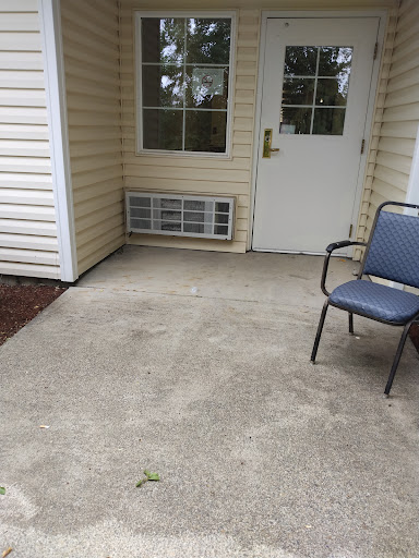 A simple outdoor entrance featuring a chair and a concrete floor.