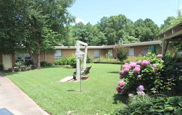 A well-maintained garden with lush green lawn, flowering bushes, and surrounding trees.