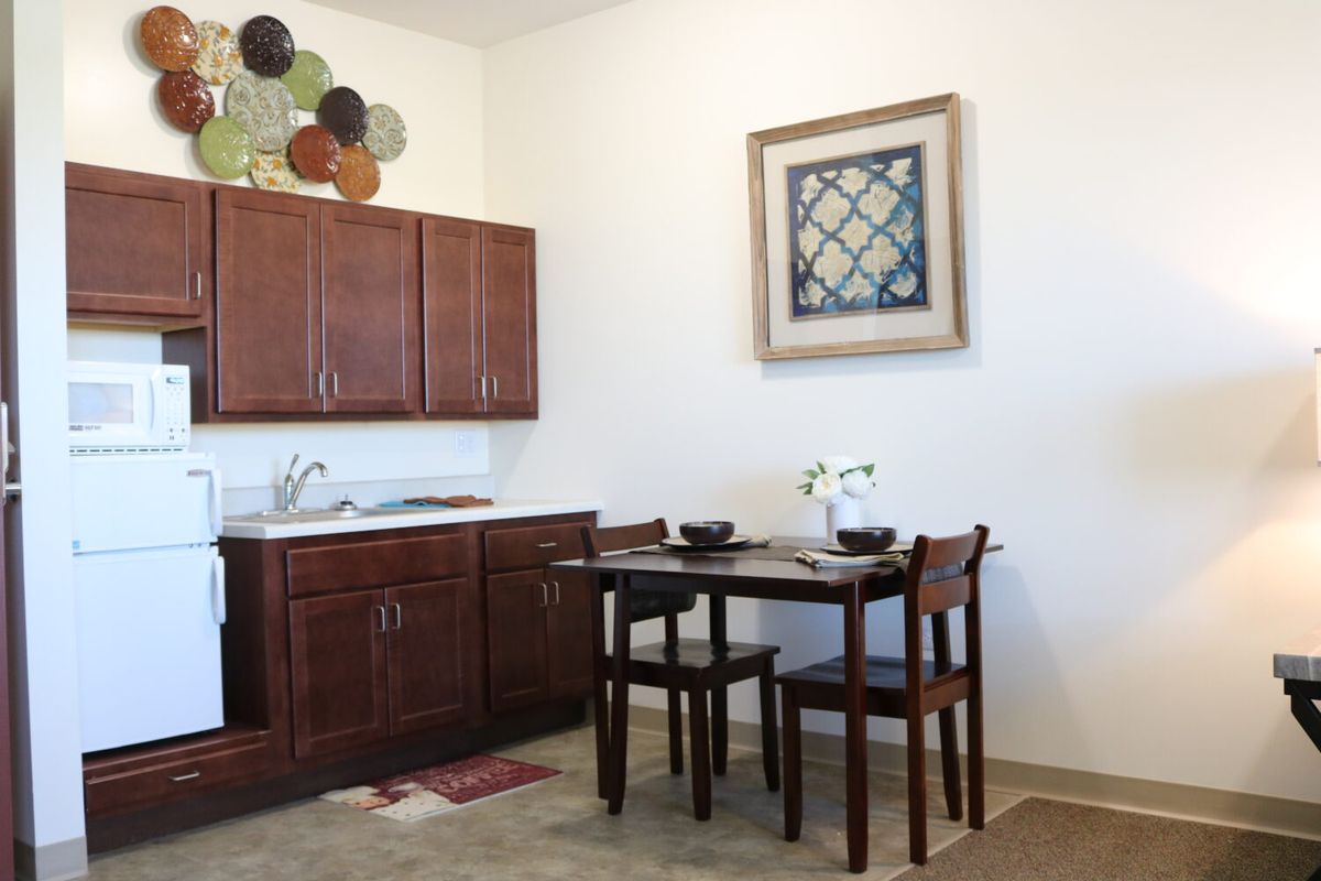 A cozy kitchen corner featuring wooden cabinets, a small dining table with two chairs, decorative plates on the wall, and framed artwork.
