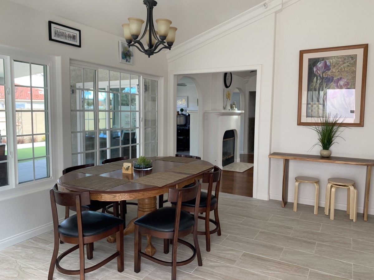 A cozy dining room with a wooden table and chairs, featuring a chandelier and glass doors leading to another room.