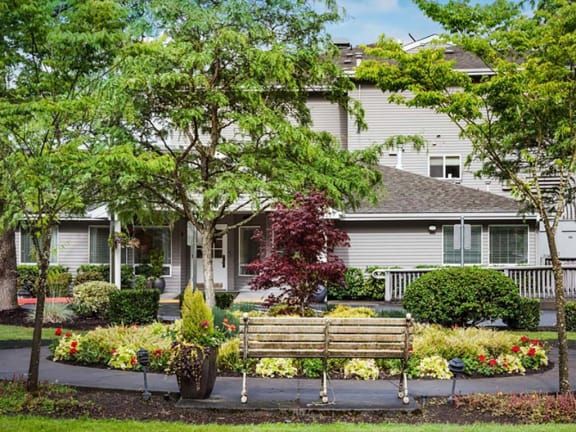 A charming house surrounded by a well-maintained garden with a wooden bench under lush trees.