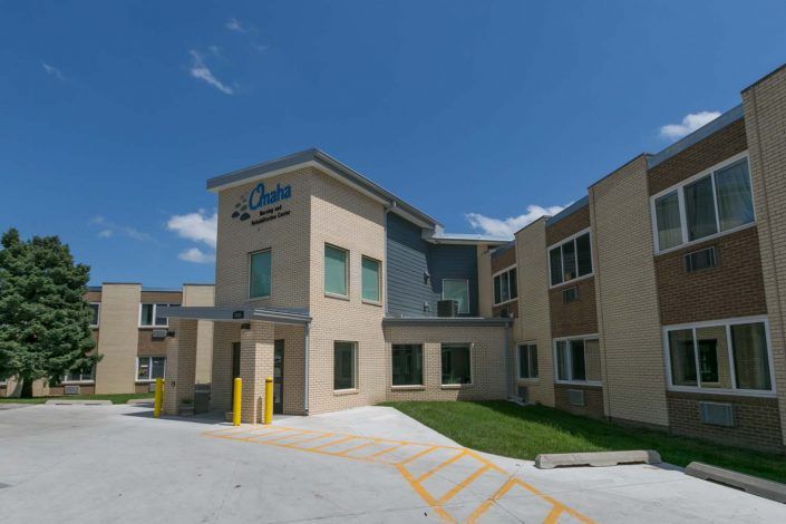 A hotel building with a modern design and parking area under a clear blue sky.