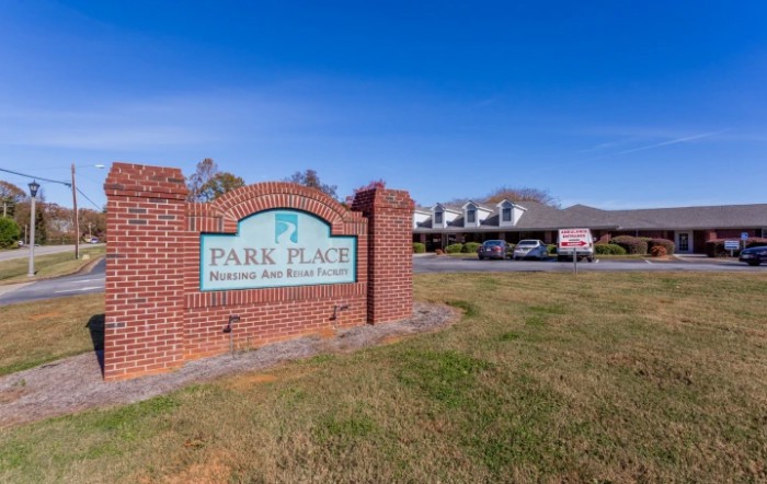 A brick sign for Park Place Apartments on a sunny day with buildings in the background.