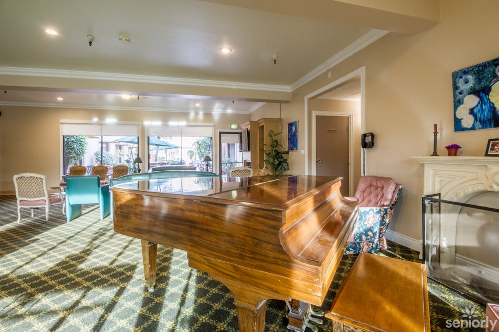 A cozy lounge area featuring a grand piano illuminated by sunlight streaming through large windows.