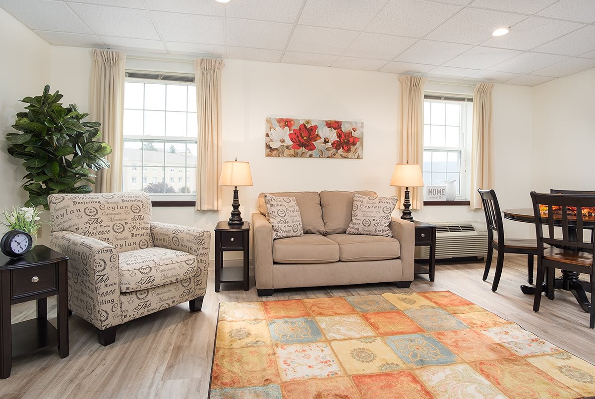 A cozy living room with a sofa, armchair, colorful rug, and decorative artwork.