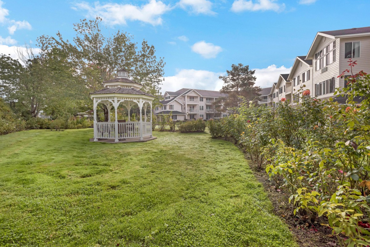 A scenic view of a garden with a gazebo and residential buildings in the background.