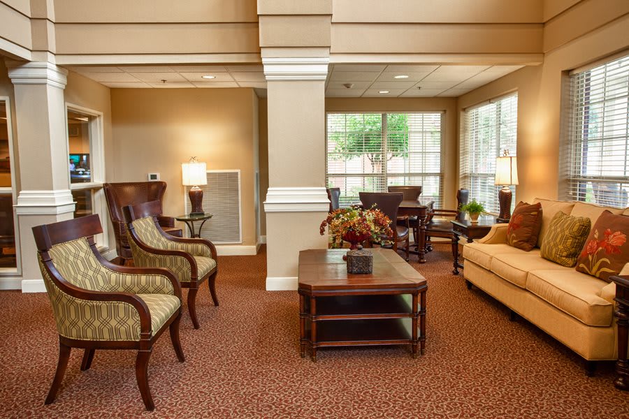 A cozy living room with elegant furniture, including chairs and a sofa, illuminated by lamps and natural light from the windows.
