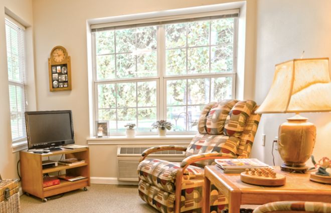 A cozy living room with an armchair by a large window and a television on a stand.