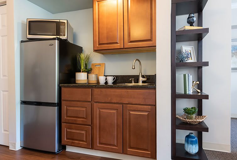 A modern kitchen area featuring wooden cabinets, a stainless steel fridge, a sink, and decorative shelves.