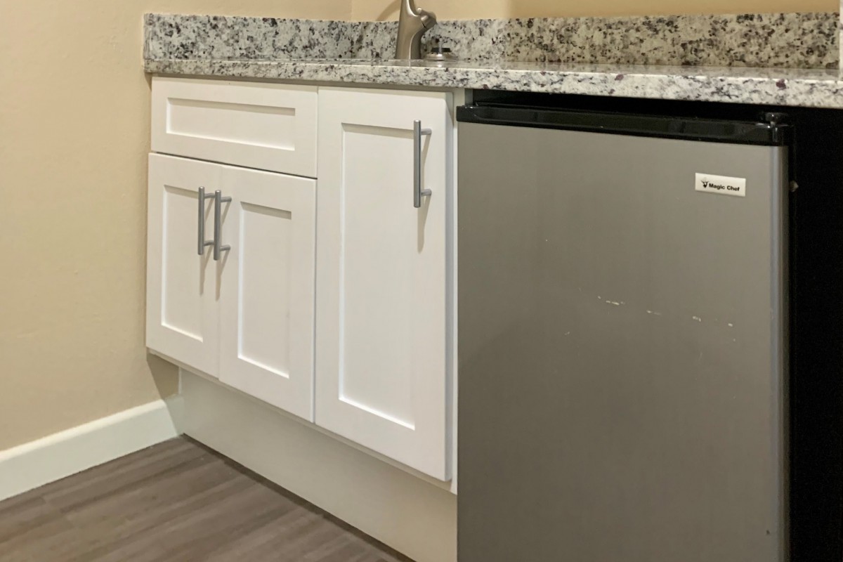 A modern kitchen area featuring white cabinets, a granite countertop, and a compact fridge.