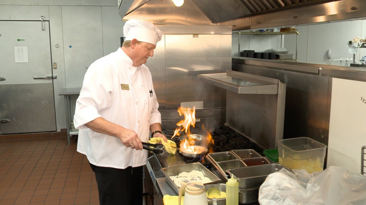 A chef cooking with a flame on a stove in a commercial kitchen.