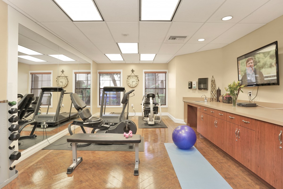 A well-lit gym with exercise equipment including treadmills, an exercise ball, and a yoga mat.