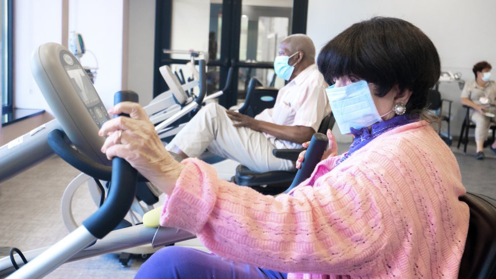 Senior citizens wearing masks and exercising on stationary bikes in a gym.