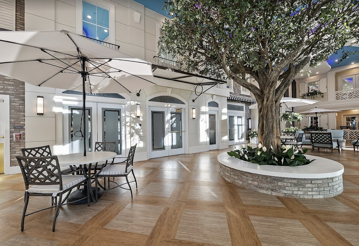 A modern indoor area with a tree, seating, and umbrellas, resembling a commercial or communal space.
