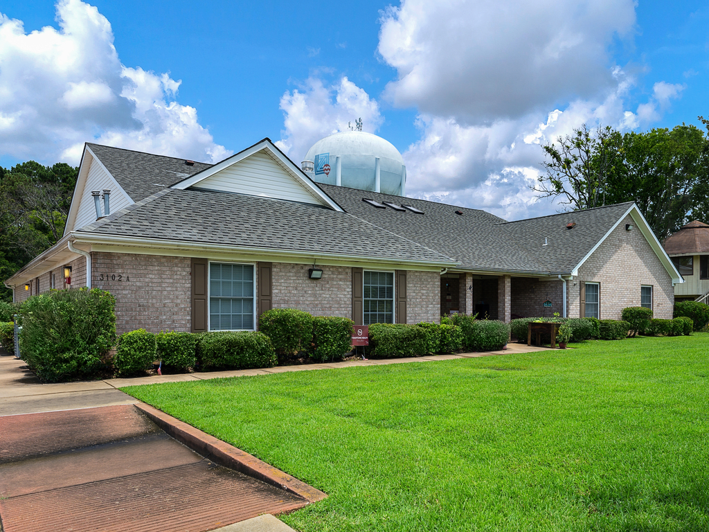 A suburban brick house with a well-maintained lawn and a clear blue sky.