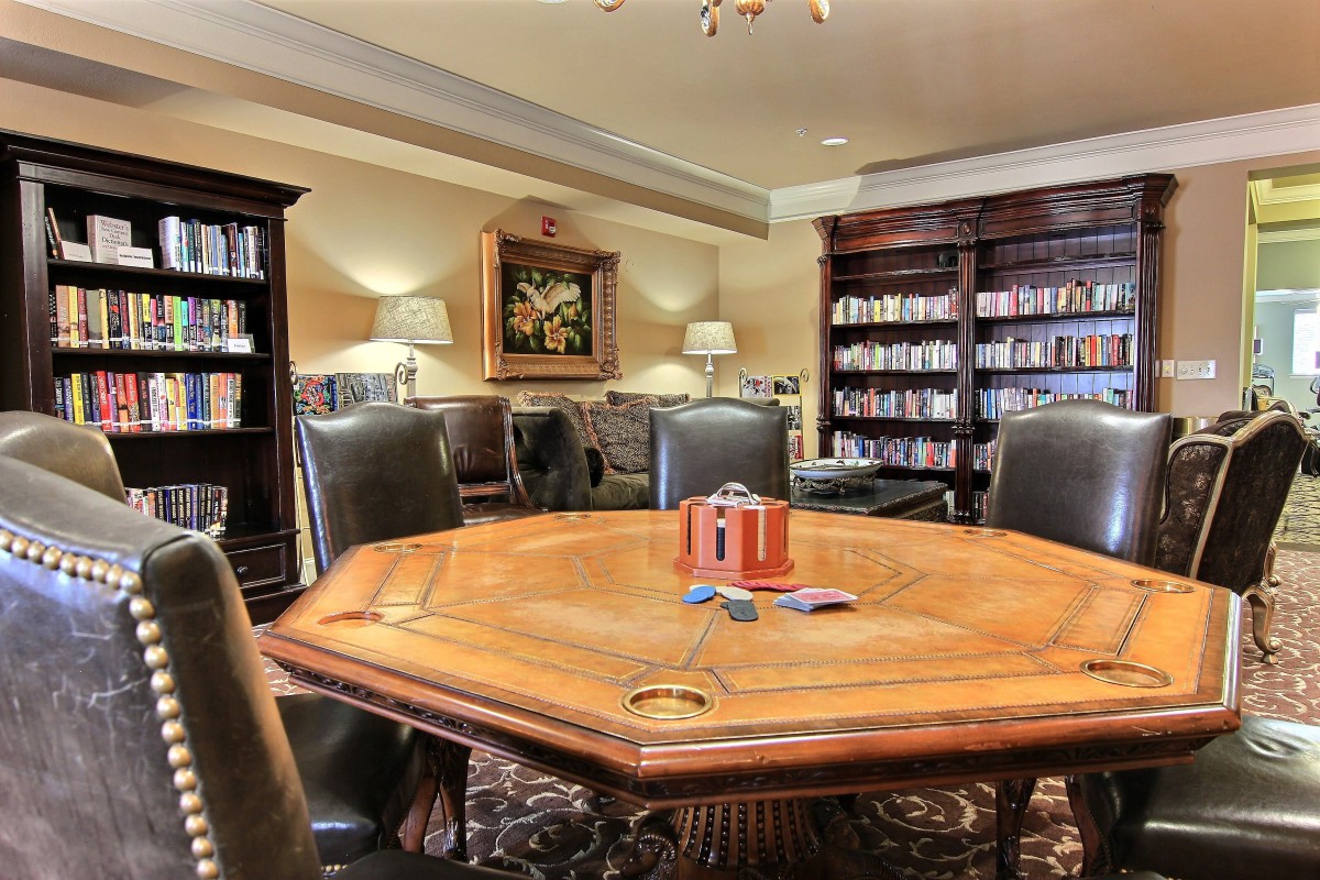 A cozy library room with a large wooden table surrounded by leather chairs and shelves filled with books.