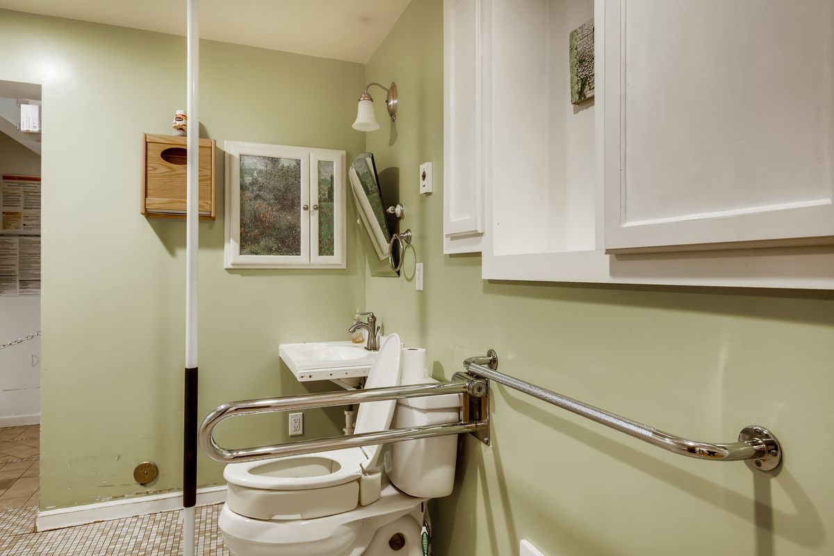 An accessible bathroom with green walls, featuring a toilet equipped with grab bars, a sink, and a mirror.