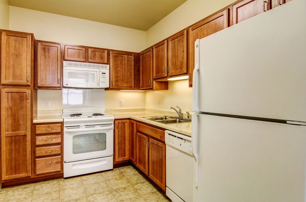 A modern kitchen featuring wooden cabinets, a refrigerator, oven, microwave, and a dishwasher.