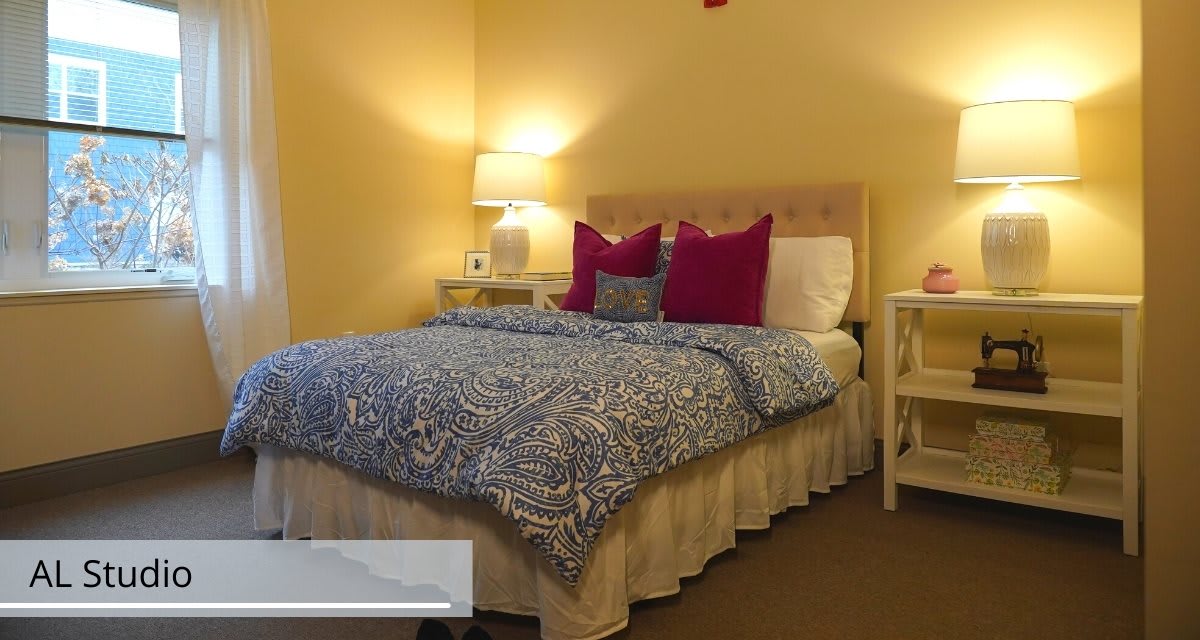 A cozy bedroom with a neatly made bed featuring patterned bedding and colorful pillows, flanked by nightstands with lamps.