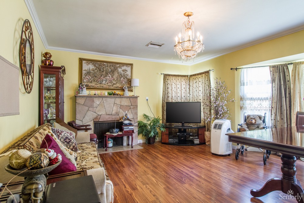 A cozy living room with hardwood floors, featuring a chandelier, sofa, fireplace, and television.