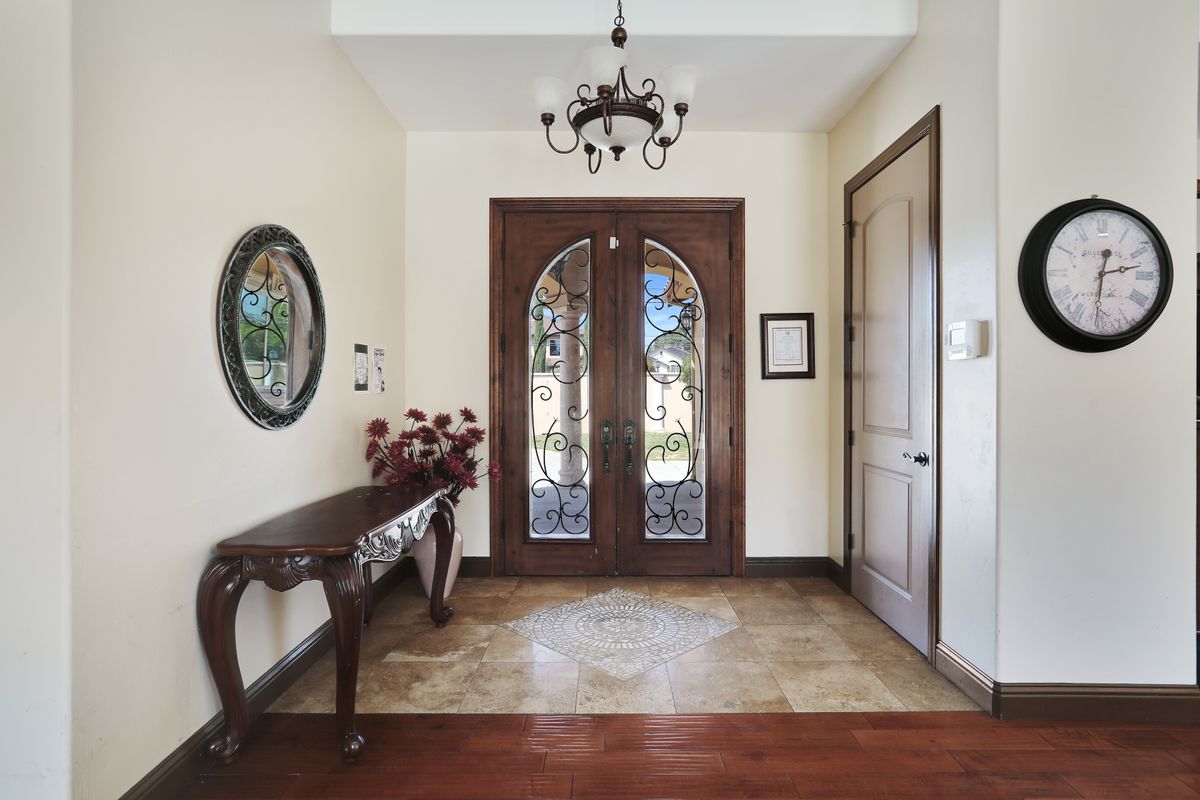 An elegant entryway with a chandelier, ornate double doors, and a decorative console table.