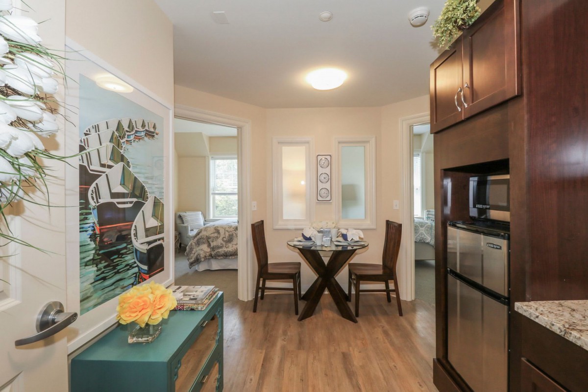 A cozy dining area with modern decor, featuring a table set for two and surrounded by vibrant artwork and wooden cabinetry.