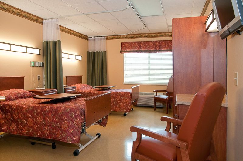 A hospital room with two beds, curtains, and chairs arranged neatly.