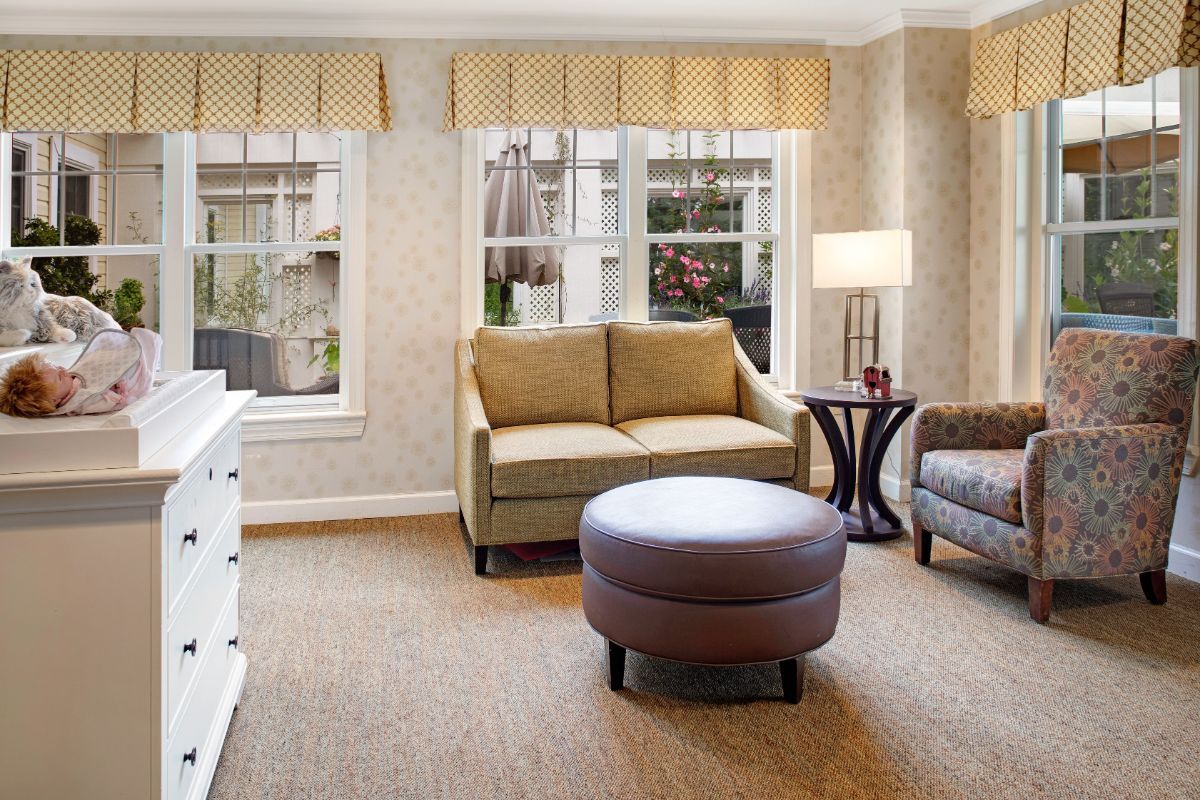 A cozy living room with a sofa, ottoman, and large windows.