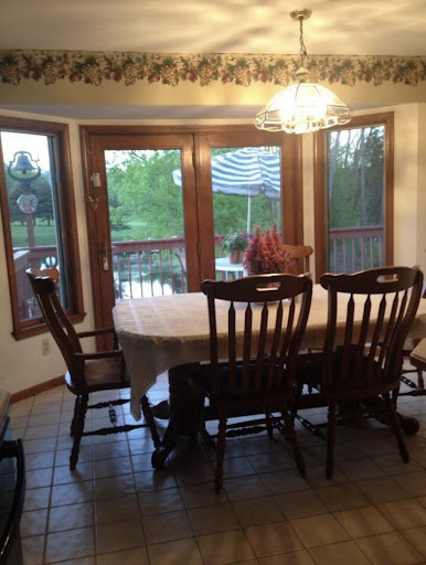 A cozy dining room featuring a wooden table and chairs, illuminated by natural light through large windows.