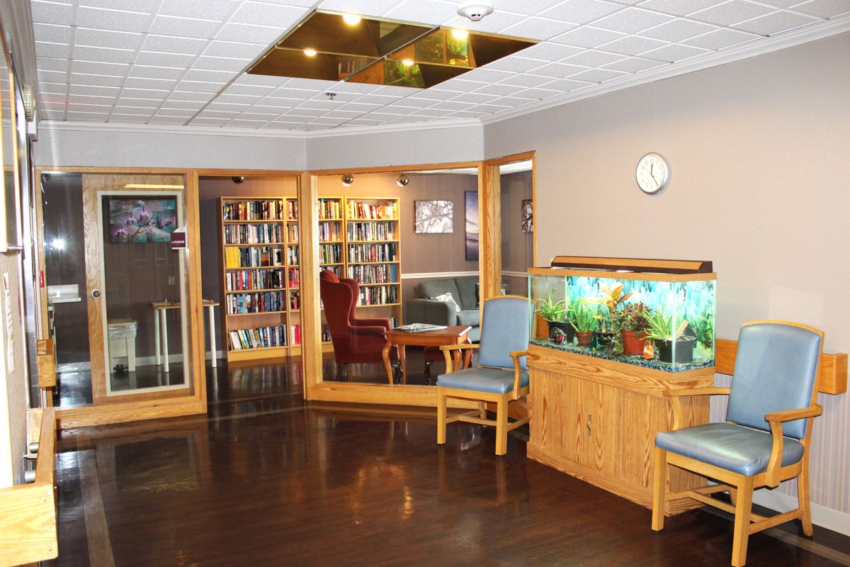 A cozy library corner with bookshelves, armchairs, and an aquarium, creating a welcoming waiting area.