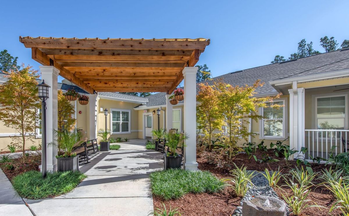 A residential building entrance with a wooden pergola and landscaped garden.