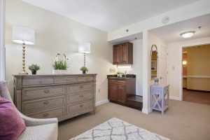 A cozy bedroom interior with a dresser, lamp, and decorative plants.