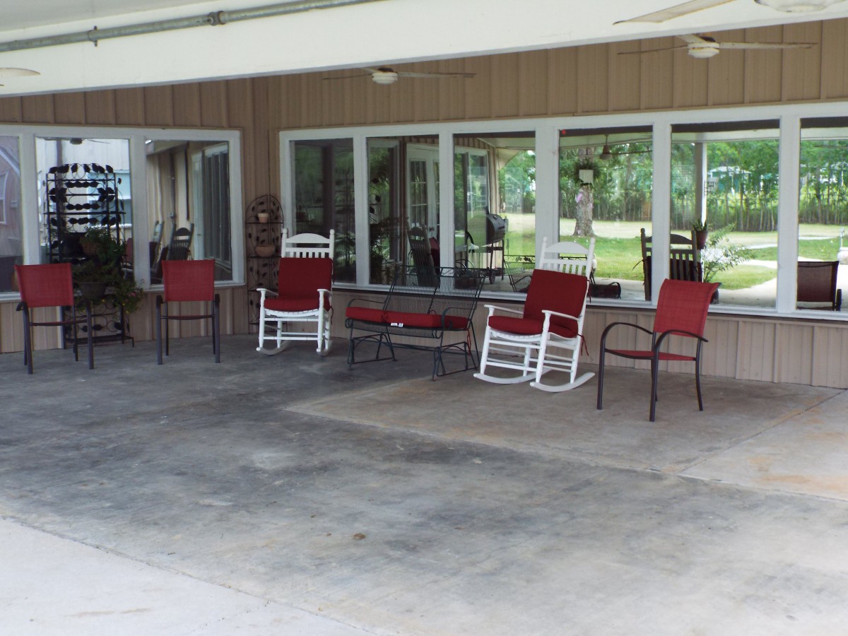 A cozy outdoor patio with red cushioned chairs and rocking chairs under a covered area.