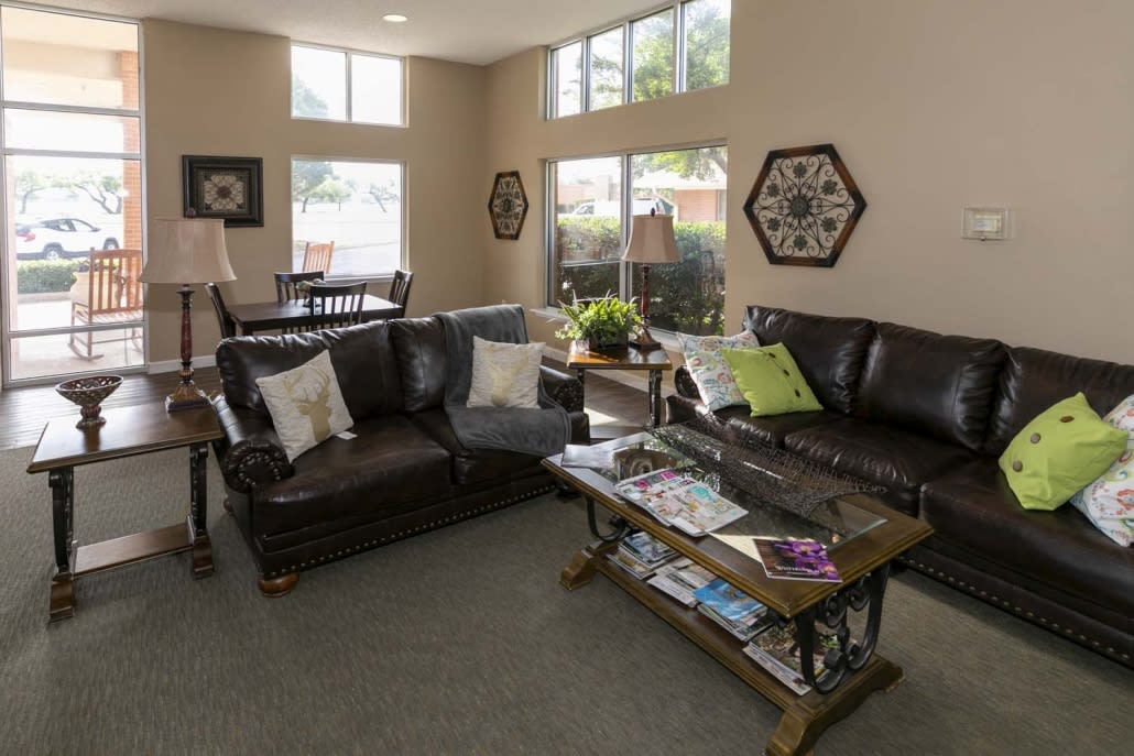 A cozy living room with leather sofas, a wooden coffee table, and large windows letting in natural light.