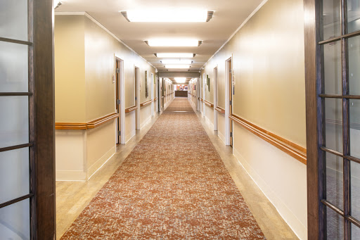 A well-lit hallway featuring carpeted flooring and lined with doors on either side.